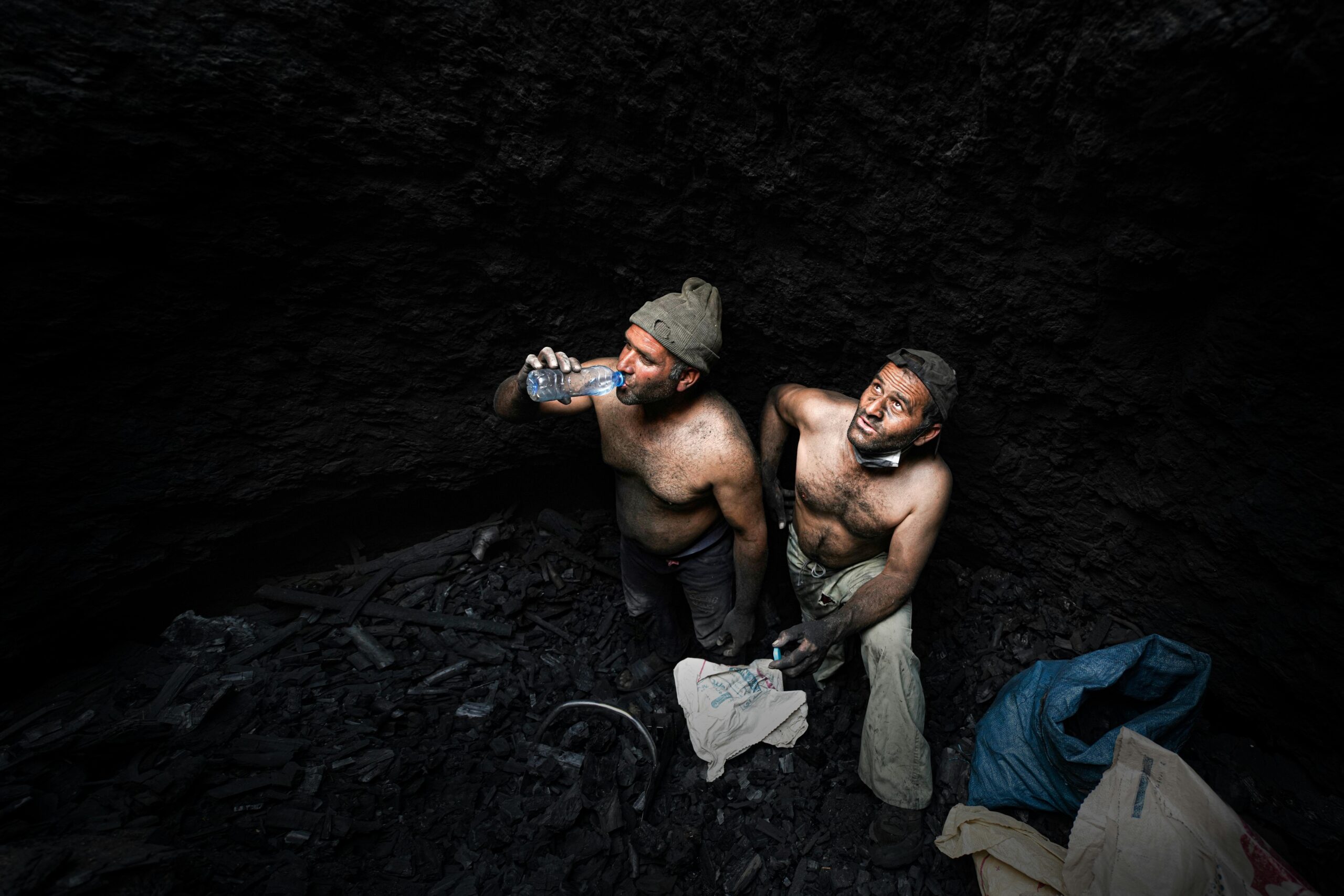 Two shirtless miners taking a break in a dark coal mine in Iran.